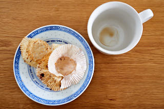 Empty plate with the rest of muffin wrapping paper next to an empty cup of coffee.
